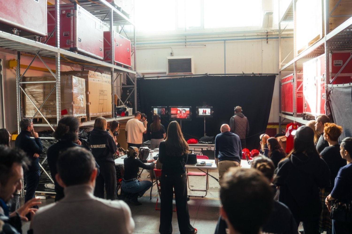 A large crew standing behind the video village in a Ferrari equipment warehouse, watching three monitors during a shoot.
