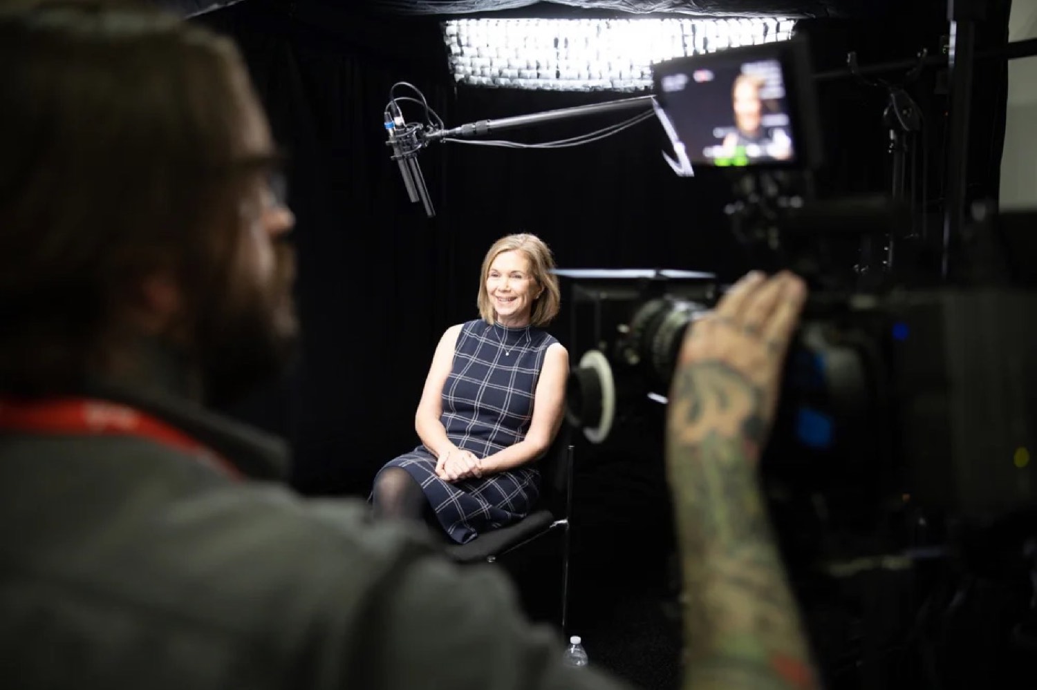 An interview subject lit against black, framed by the camera operator's shoulder and an overhead boom.