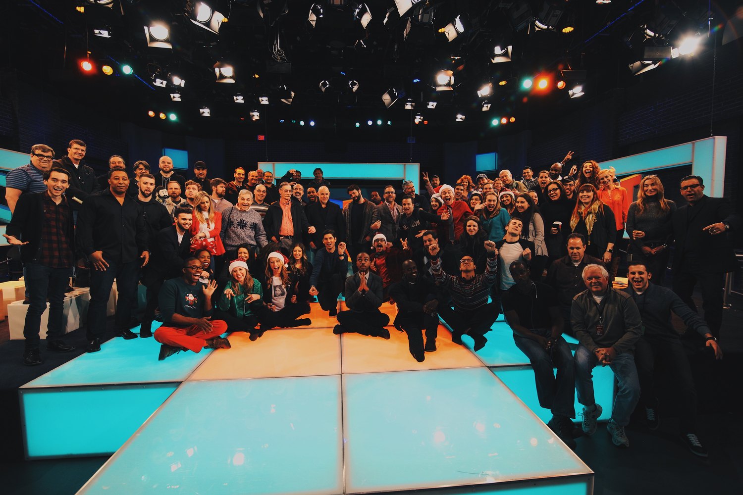 A full television crew of roughly eighty people gathered on a lit studio set at the end of a shoot day.