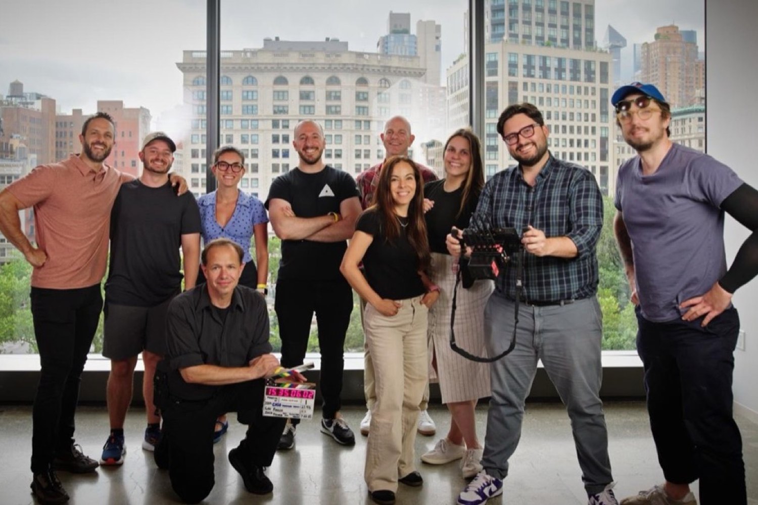 The full crew posed with the slate in front of a window wall over Manhattan at the end of the shoot day.