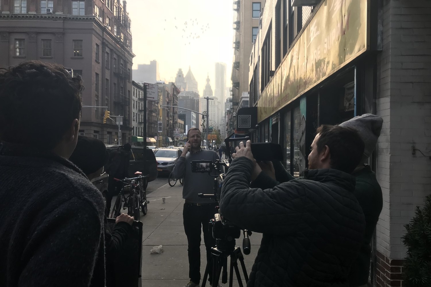 A street scene shot in Lower Manhattan at golden hour: an actor on a phone call mid-sidewalk, two operators working the frame.
