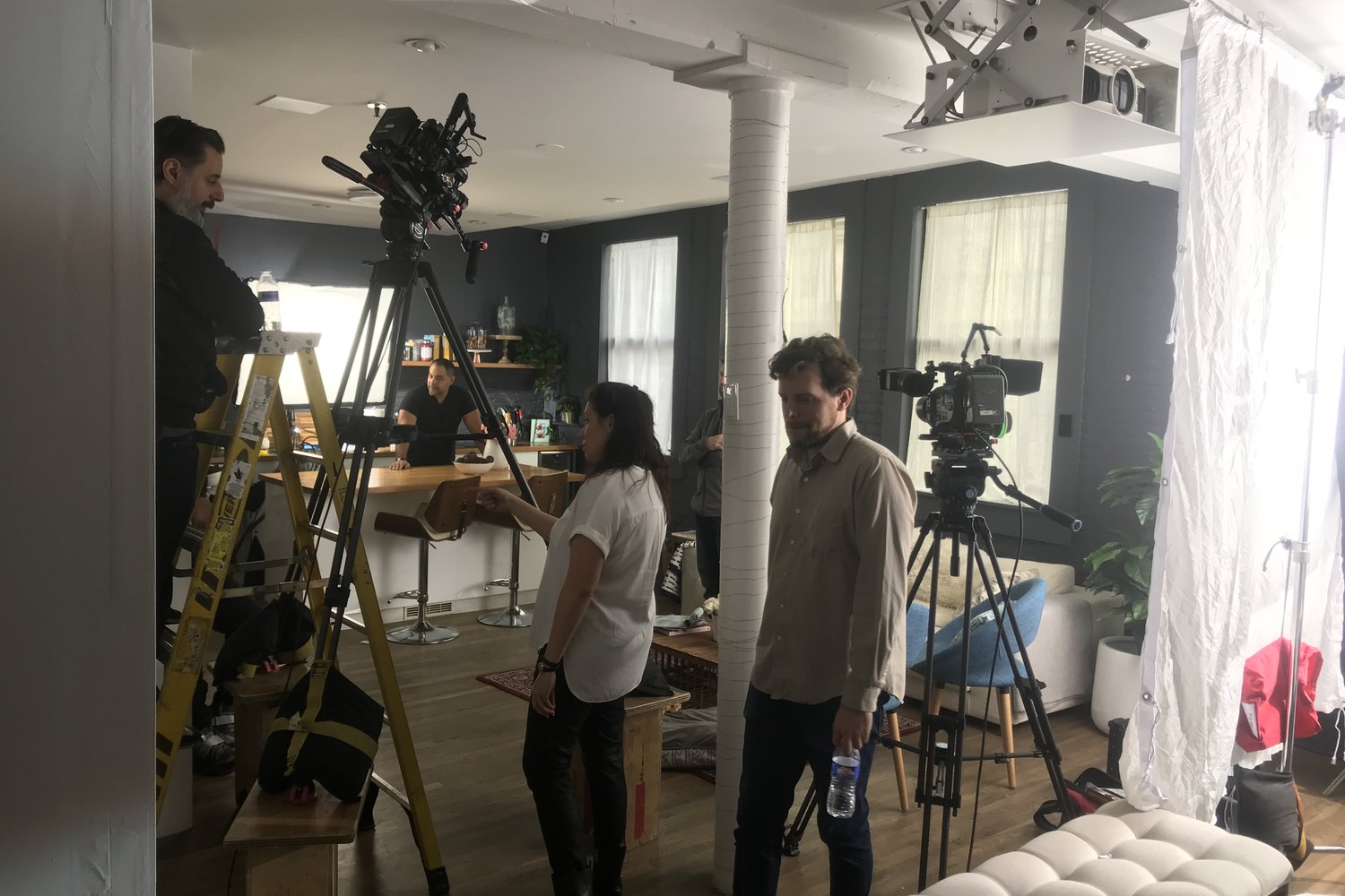 A loft built as a location: ladder, dolly and camera rigged, crew and cast working through a scene.
